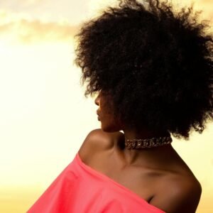 An elegant woman with Afro hair in a pink top at sunset, creating a dramatic silhouette.